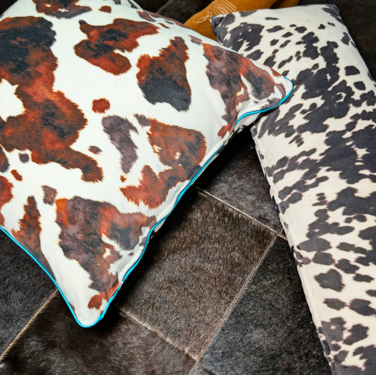 Two spotted cow print pillows on a brown cowhide rug